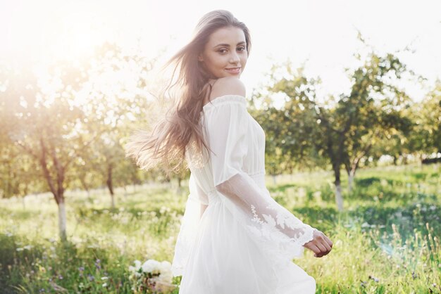 Photo a young girl in a white long dress is walking in the garden beautiful sunset through the leaves of trees