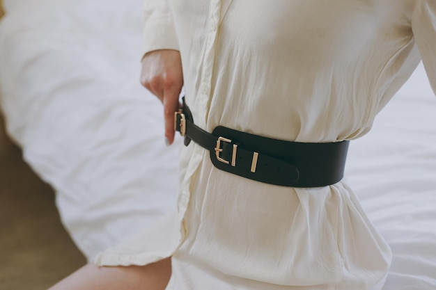 Young girl in a white office shirt trying on a leather belt