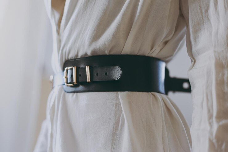 Young girl in a white office shirt trying on a leather belt