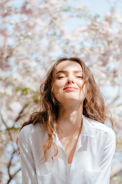 白いシャツを着た少女が花の咲く桜の近くで撮影されています