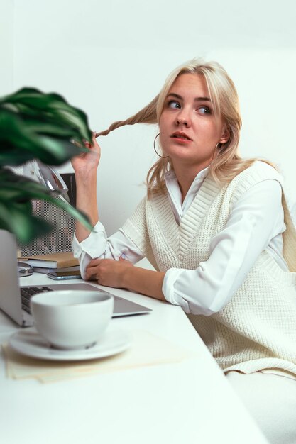 La ragazza si avvolge i capelli su un dito con un viso pensieroso a un tavolo da lavoro