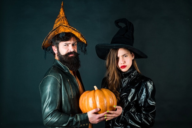 Photo young girl witch in halloween hat and bearded man over black background. halloween design for copy space. cute man and woman wearing halloween clothes.