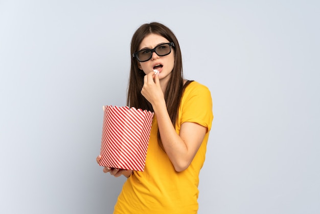 Молодая девушка в 3d-очках и держит большое ведро попкорна, глядя в сторону
