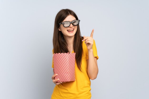 Young girl with 3d glasses and holding a big bucket of popcorns while pointing front