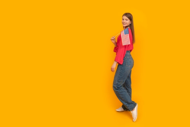 Young girl with an american flag in her hands fulllength portrait of teenager on yellow background copy space