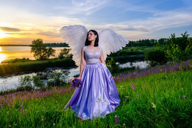 野生の花の花束と牧草地に座っている天使の翼を持つ少女