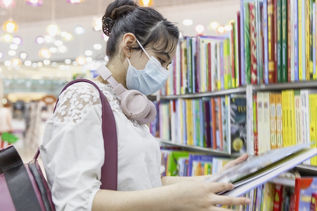 A young girl with a backpack and in headphones selects a book on the shelves in the store