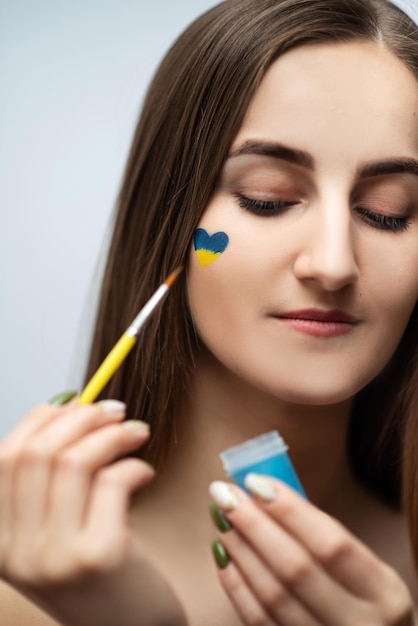 A young girl with beautiful skin draws a heart from the colors of the Ukrainian flag no war