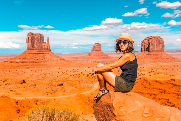 A young girl with black t-shirt sitting in the center of the photo on a stone in the Monument Valley National Park