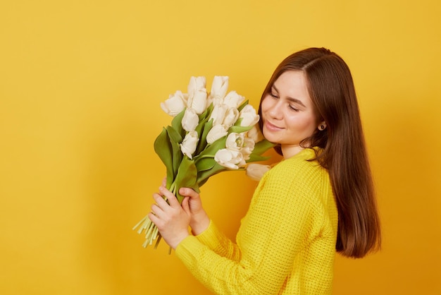 Young girl with a bouquet of white tulips on a yellow background