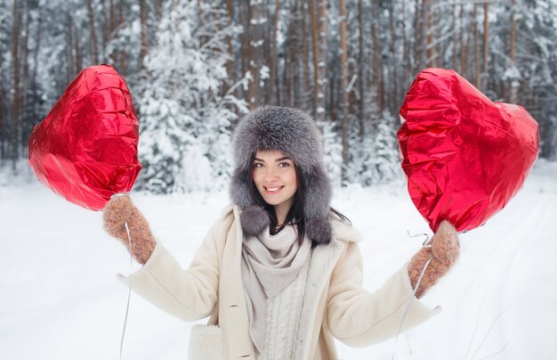 雪に覆われた森の中に、ハート型の風船を持った少女が立っています。バレンタイン・デー。冬休みに。