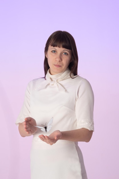 Photo a young girl with butterfly in arm. woman in white clothes on a pale pink background with butterfly.