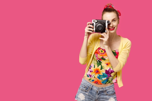ピンクの背景の笑顔に手でカメラを持つ少女