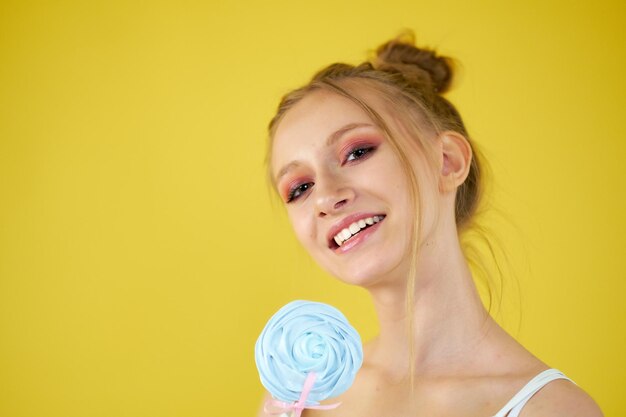 Photo young girl with candy on a yellow bright background beautiful makeup