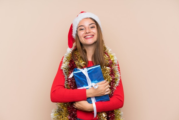 Young girl with christmas hat holding a gift over isolated wall