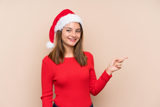 Ragazza con il cappello di natale sopra fondo isolato che indica dito il lato