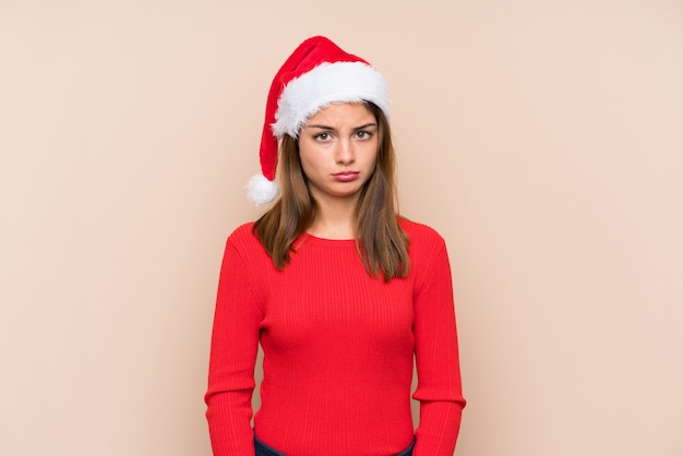 Young girl with christmas hat over isolated wall sad