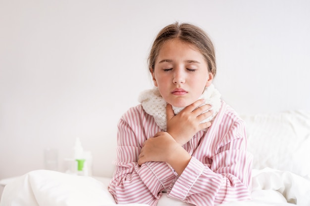 Young girl with a cold sits on her bed