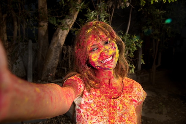 Young girl with colorful face taking selfie using smartphone on Holi festival