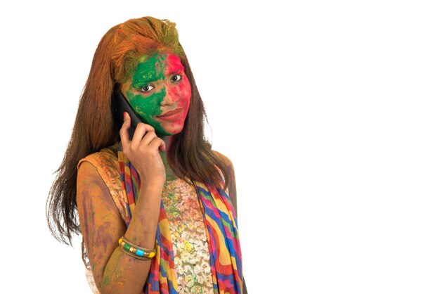 Young girl with colorful face talking on phone and celebrating festival of color Holi.