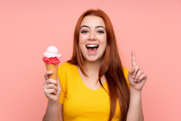 Young girl with a cornet ice cream over isolated wall pointing up a great idea