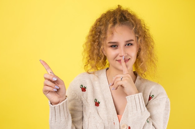 A young girl with curly hair points with a gesture on a studio background