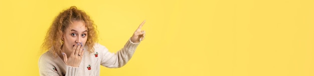 A young girl with curly hair points with a gesture on a studio background