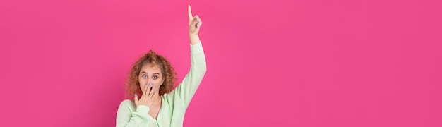 A young girl with curly hair points with a gesture on a studio background