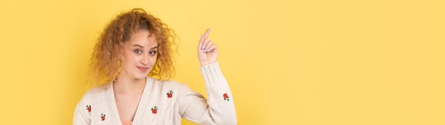 A young girl with curly hair points with a gesture on a studio background