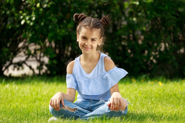 A young girl with dark hair in a blue shirt and jeans sits in the park in the summer. High quality photo