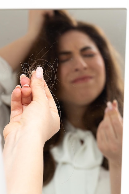 Young girl with a disgusted look who looking at herself in the mirror observes a lock of hair between her fingers Trichotillomania disorder a compulsive mania in which hair and hair are pulled out