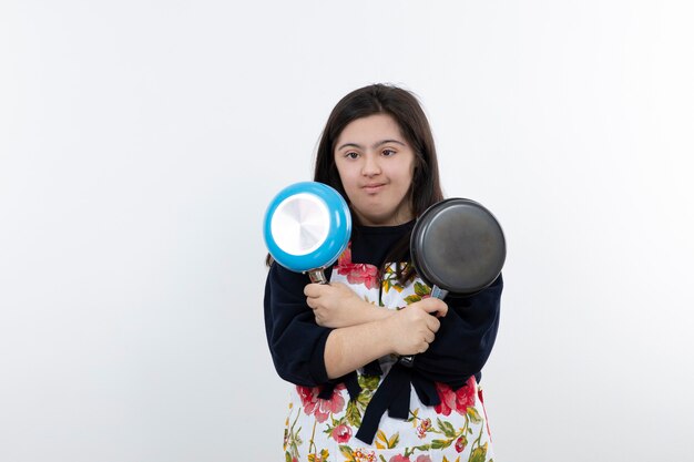 young girl with down syndrome in apron holding frying pans.