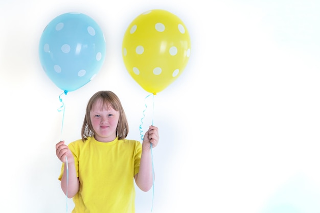 Giovane ragazza con sindrome di down che tiene due palloncini blu e gialli isolati su sfondo bianco