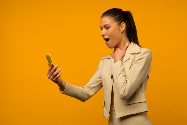 Young girl with facial skin problems posing with a smartphone on a yellow background.