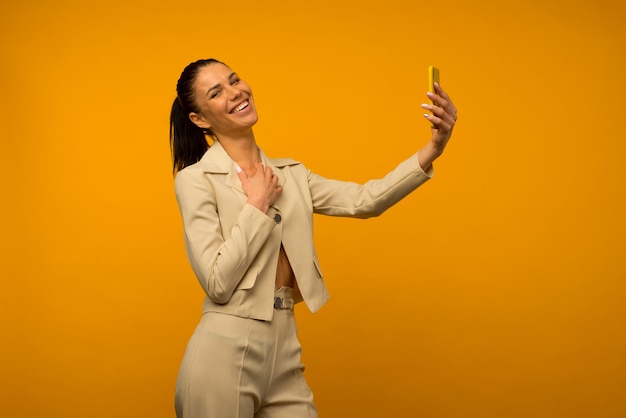 Young girl with facial skin problems posing with a smartphone on a yellow background.