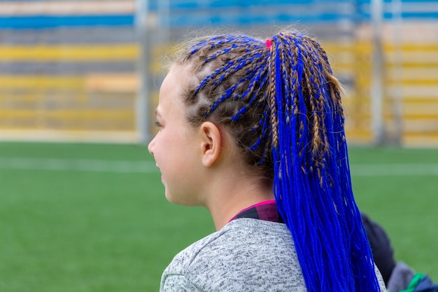 Young girl with fashionable hairstyle with braided blue ribbons in her hair, blue hair. Unusual hairstyle