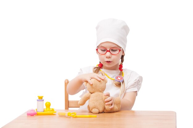 Young girl with glasses plays in the doctor as a mom and treats toys