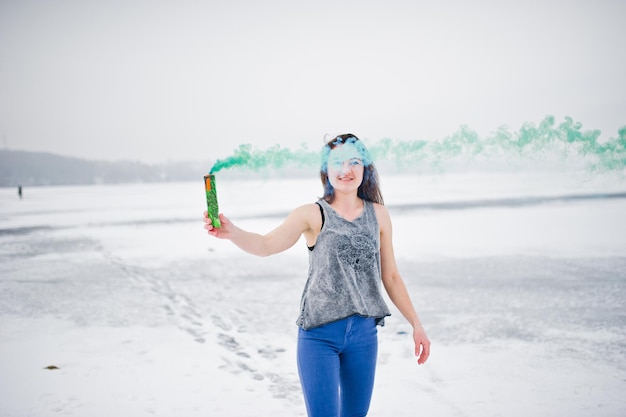 Молодая девушка с зеленой дымовой шашкой в руке в зимний день