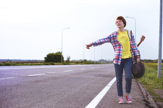 Young girl with a guitar coming along the road and hitch-hiking