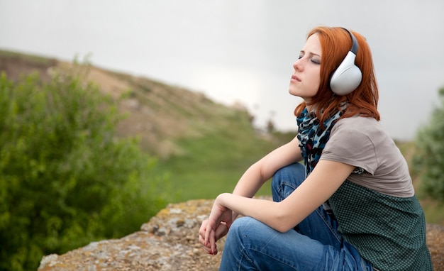 Young girl with headphones sitting on a bank of lake.