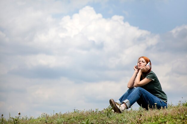 Young girl with headphones sitting on a bank of lake.