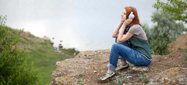 Young girl with headphones sitting on a bank of lake.