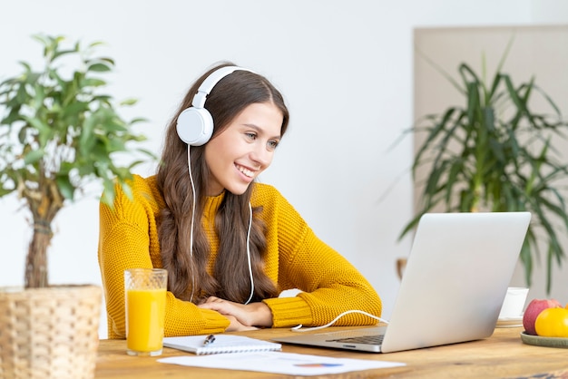 Young girl with headphones talking on conference calls, waving hand, smiling.