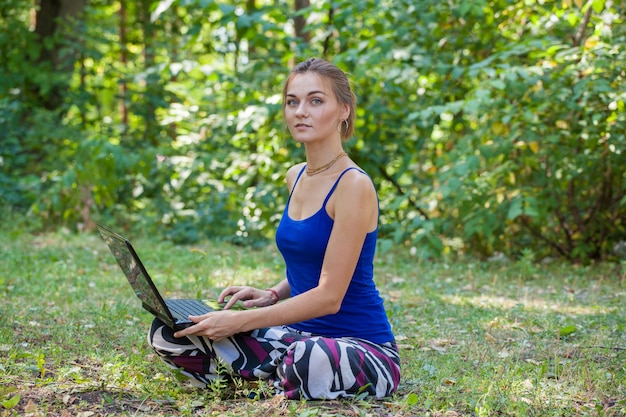 Young girl with laptop on the grass in the park