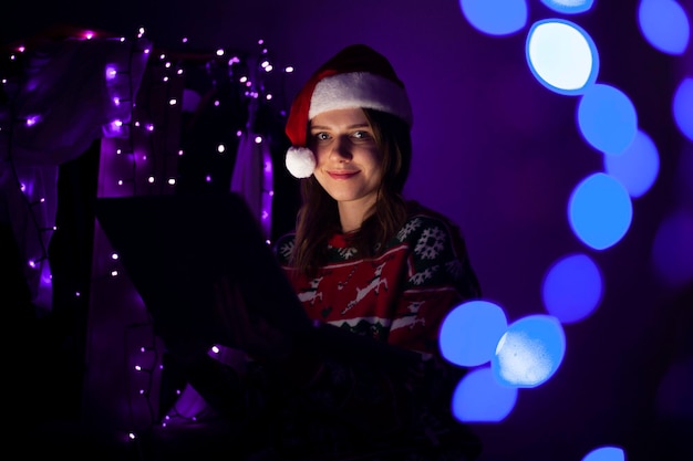 Young girl with a laptop in the New Year sits at home in Christmas clothes