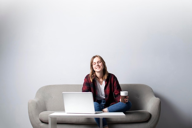 Young girl with a laptop sitting on the couch and drinking coffee a woman using a computer