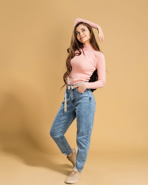 Young girl with long curly hair in a pink sweatshirt posing on a pastel orange