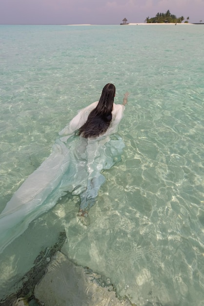 Young girl with long hair in white dress in turquoise aqua mint blue water of the ocean in the maldives
