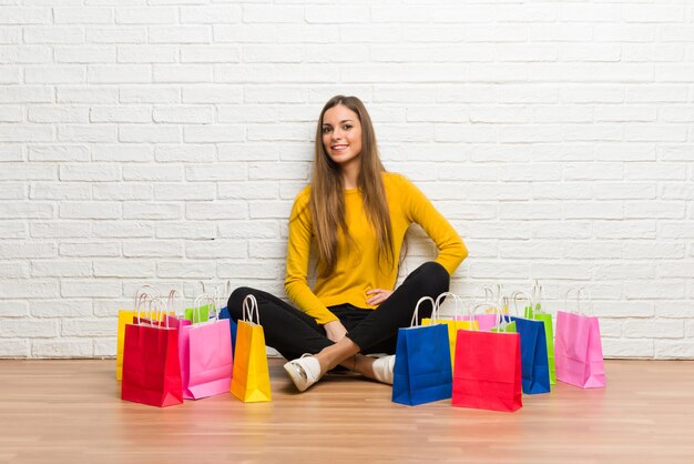 Young girl with lot of shopping bags posing with arms at hip and smiling