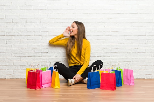 Young girl with lot of shopping bags shouting with mouth wide open to the lateral